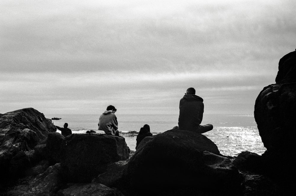 silhouette of people sitting on rock near body of water