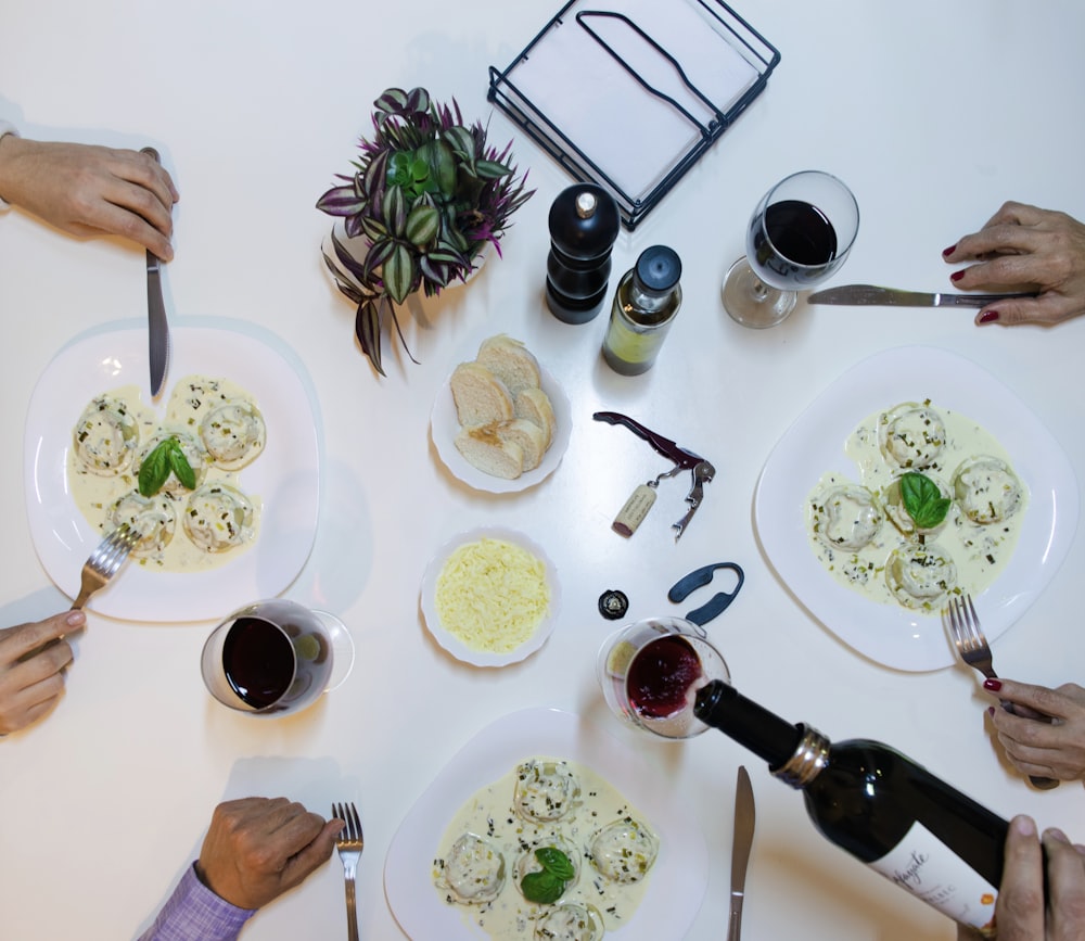 person holding bottle pouring wine on drinking glasses