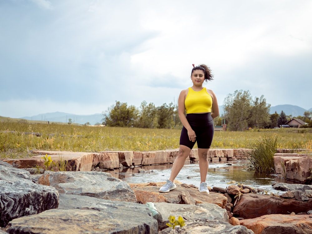 woman in yellow tank top and black shorts standing on brown rock during daytime