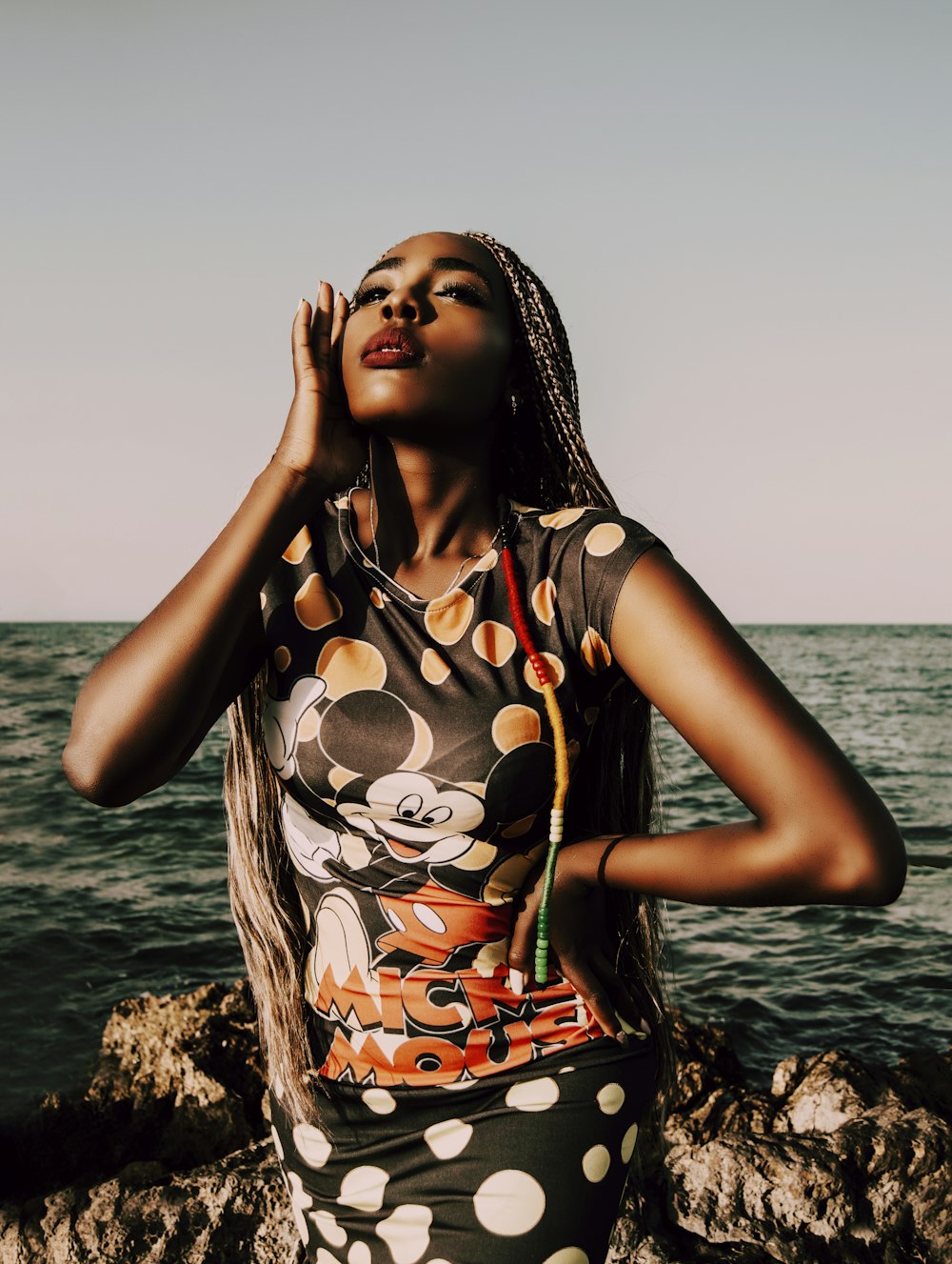 woman in black and red floral dress standing on rock near body of water during daytime