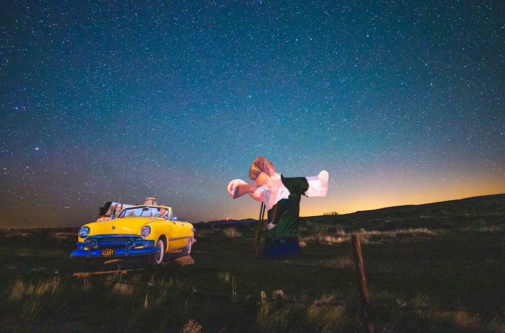 man in white shirt and black pants standing beside yellow car during night time