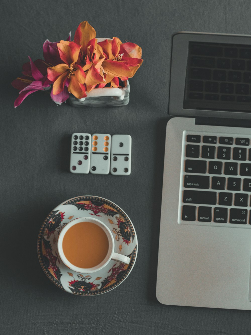 white remote control beside white ceramic mug on saucer beside macbook pro