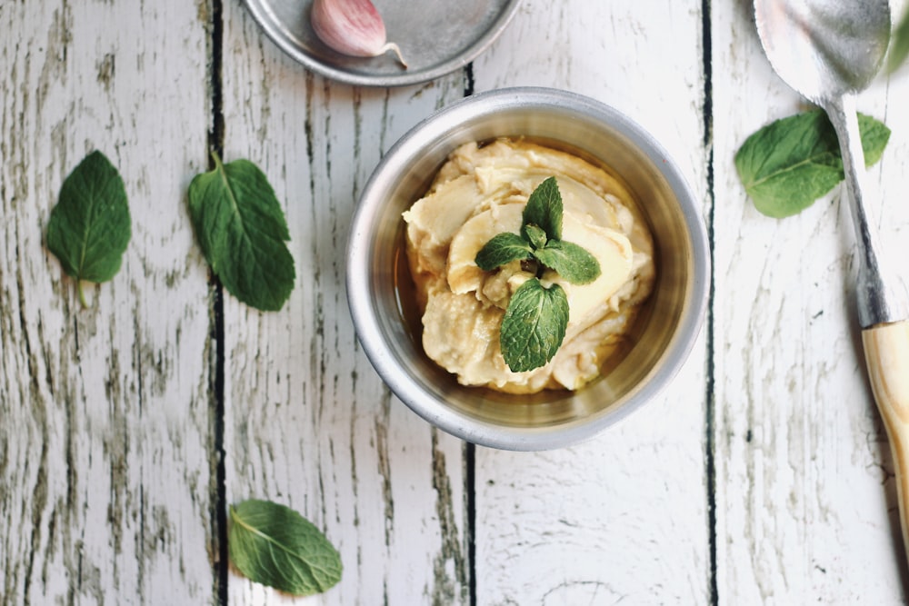 white ceramic bowl with soup beside green leaves