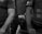 Three individuals in protective gear are partially visible, with one in the center holding a small canister. Their attire suggests a law enforcement or security role, and the image has a serious mood.