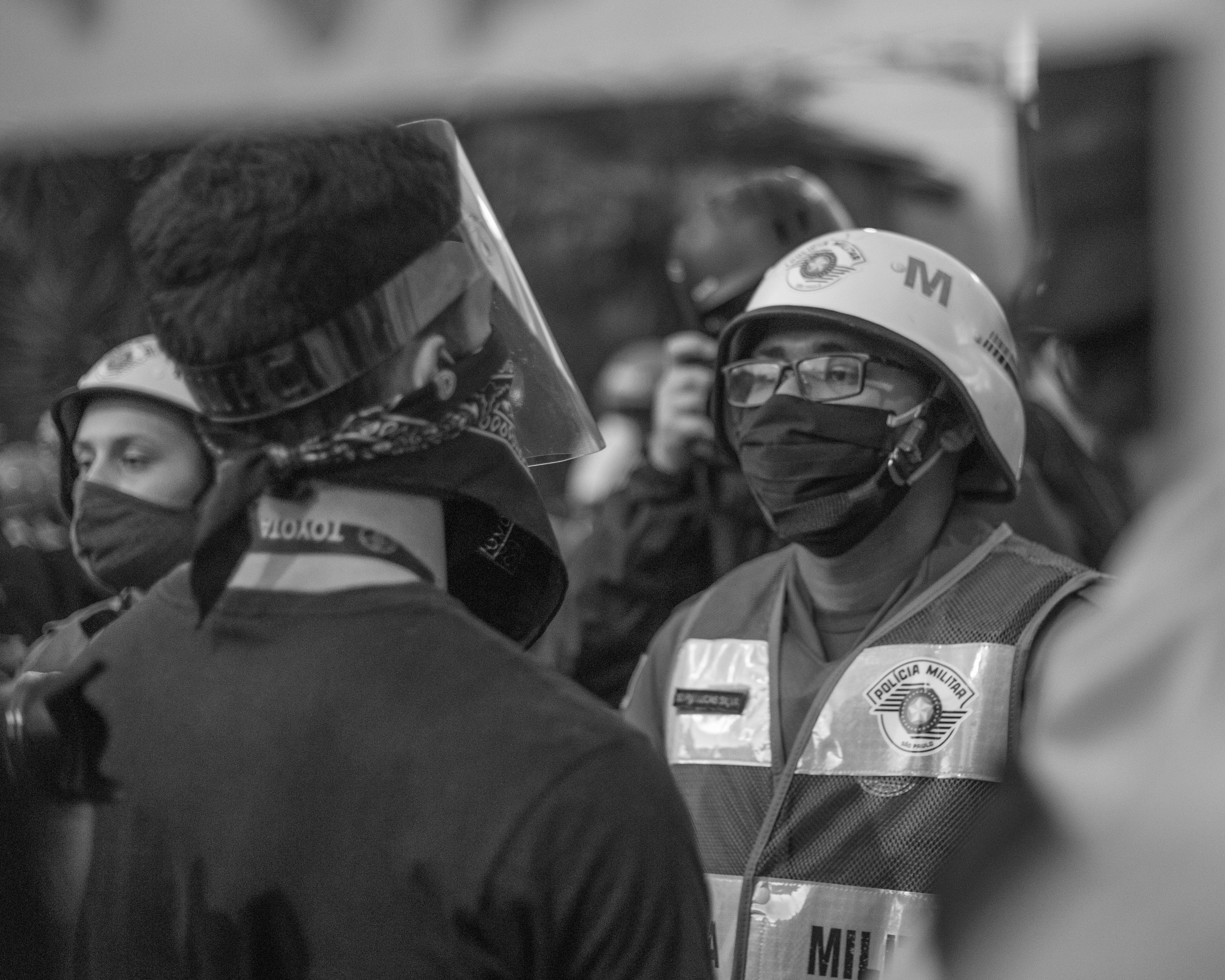 grayscale photo of man in police uniform, protester in front of police officers