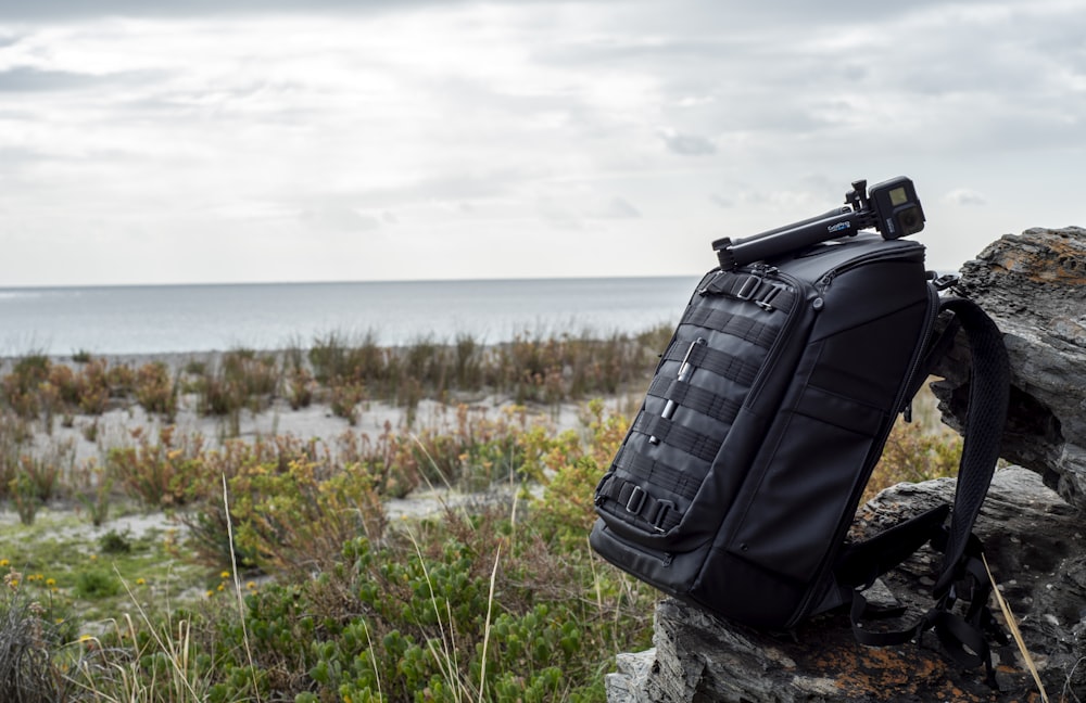 black backpack on gray rock near body of water during daytime