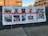 A large banner with images of individuals, alongside details such as their names, dates of death, ages, and associated incidents. It displays messages advocating for systemic change and economic equality. The banner is attached to a fence, with buildings visible in the background.