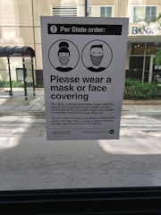 A notice posted inside a vehicle provides information about a state executive order requiring individuals to wear masks or face coverings. The notice includes two illustrated figures with masks and instructs the public to comply to help stop the spread of COVID-19.