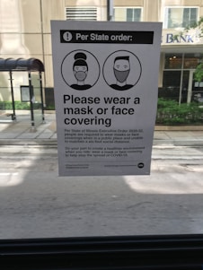 A notice posted inside a vehicle provides information about a state executive order requiring individuals to wear masks or face coverings. The notice includes two illustrated figures with masks and instructs the public to comply to help stop the spread of COVID-19.