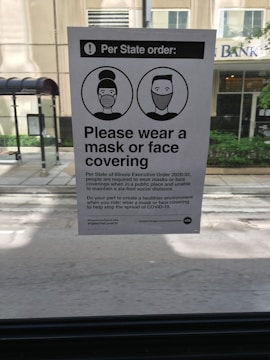 A notice posted inside a vehicle provides information about a state executive order requiring individuals to wear masks or face coverings. The notice includes two illustrated figures with masks and instructs the public to comply to help stop the spread of COVID-19.