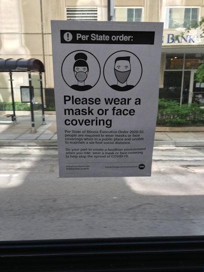 A notice posted inside a vehicle provides information about a state executive order requiring individuals to wear masks or face coverings. The notice includes two illustrated figures with masks and instructs the public to comply to help stop the spread of COVID-19.