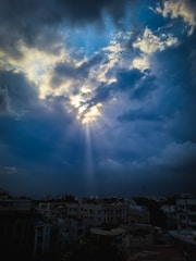 A bright ray of light breaking through a dark cloud over a city skyline.