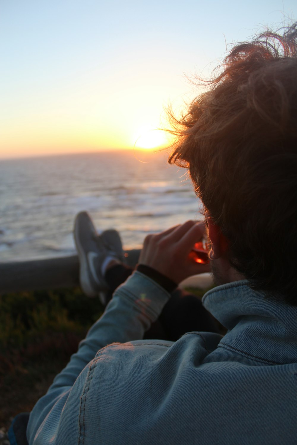 person in blue denim jacket near body of water during sunset