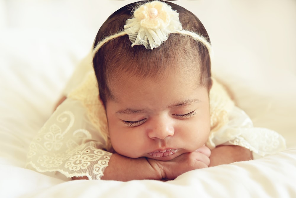 baby in white dress lying on white textile