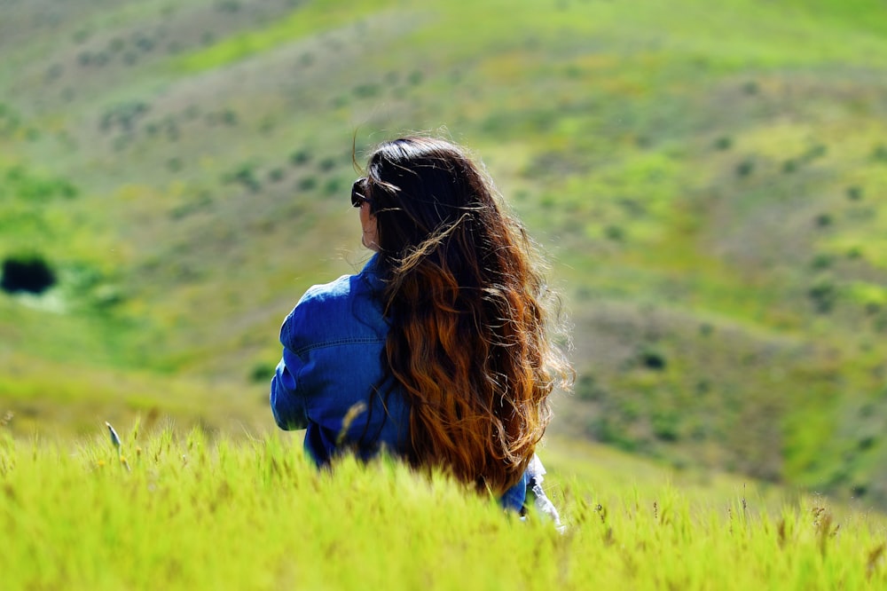 woman in blue jacket sitting on green grass field during daytime