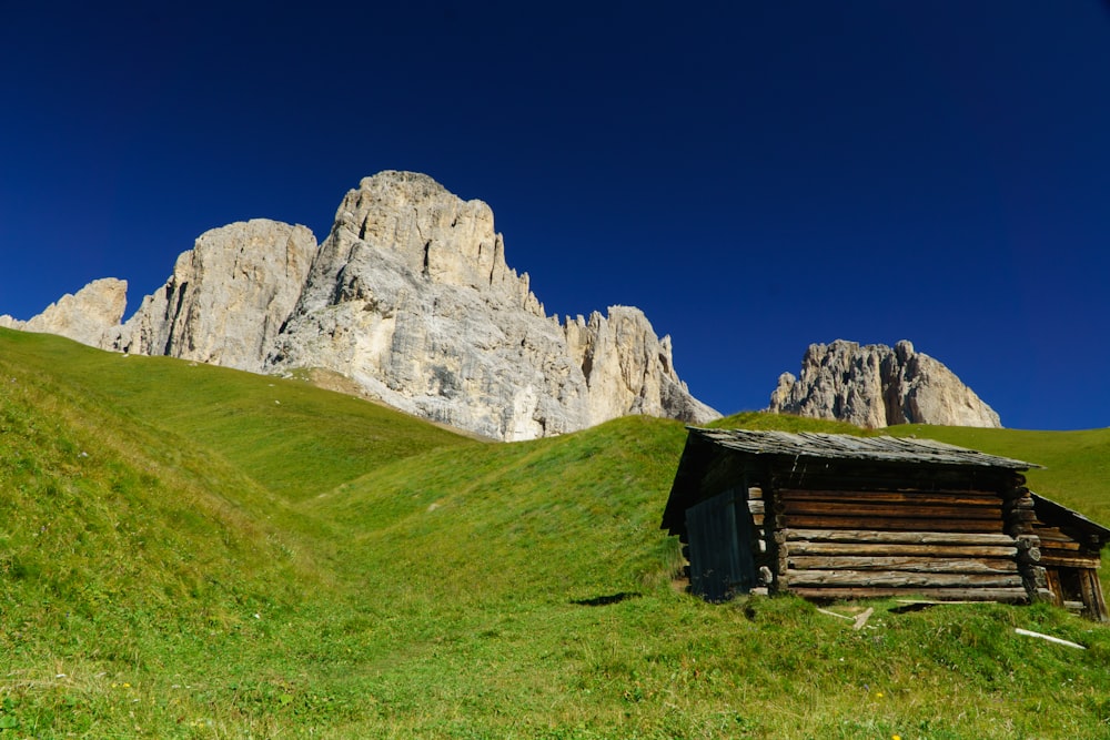 brown wooden house on green grass field near gray rocky mountain under blue sky during daytime
