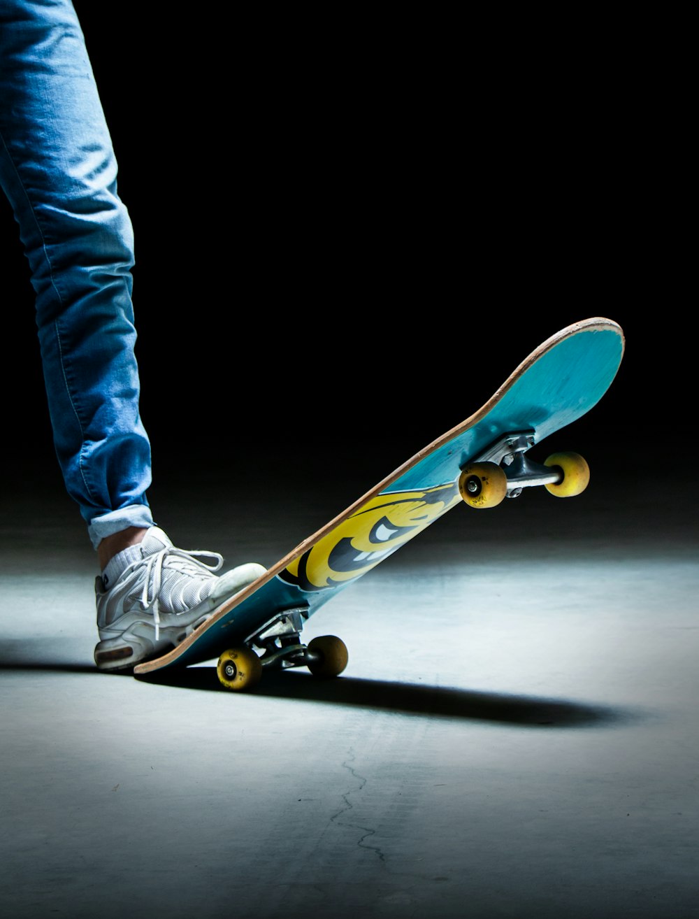 Persona in jeans blu denim e scarpe da ginnastica Nike in bianco e nero che cavalcano lo skateboard