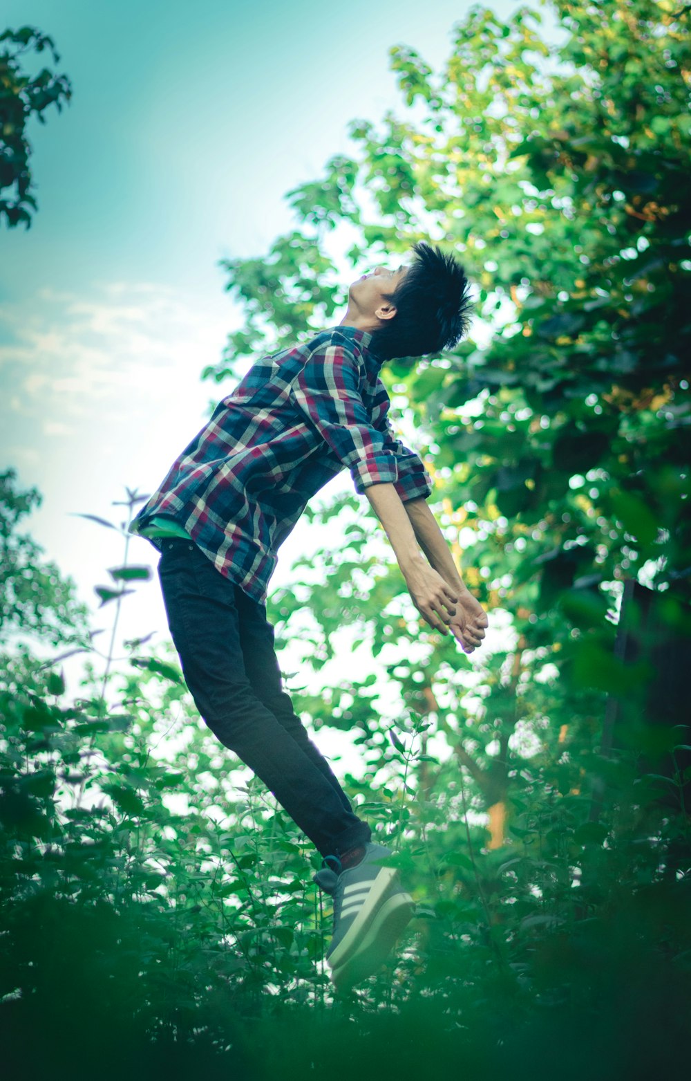 man in red and black plaid dress shirt and black pants jumping on green grass field