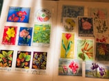 A collection of international postage stamps featuring a variety of floral designs, displayed on an album page. The stamps showcase vibrant images of flowers, including roses, daffodils, tulips, and other botanical illustrations, with inscriptions in various languages. Some stamps have been postmarked, indicating past usage.