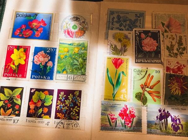 A collection of international postage stamps featuring a variety of floral designs, displayed on an album page. The stamps showcase vibrant images of flowers, including roses, daffodils, tulips, and other botanical illustrations, with inscriptions in various languages. Some stamps have been postmarked, indicating past usage.