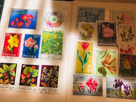 A collection of international postage stamps featuring a variety of floral designs, displayed on an album page. The stamps showcase vibrant images of flowers, including roses, daffodils, tulips, and other botanical illustrations, with inscriptions in various languages. Some stamps have been postmarked, indicating past usage.