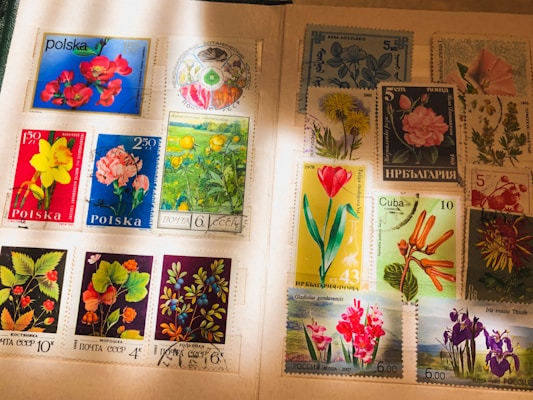 A collection of international postage stamps featuring a variety of floral designs, displayed on an album page. The stamps showcase vibrant images of flowers, including roses, daffodils, tulips, and other botanical illustrations, with inscriptions in various languages. Some stamps have been postmarked, indicating past usage.