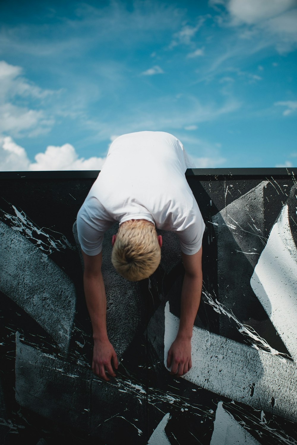 man in white t-shirt and gray shorts sitting on gray concrete wall during daytime