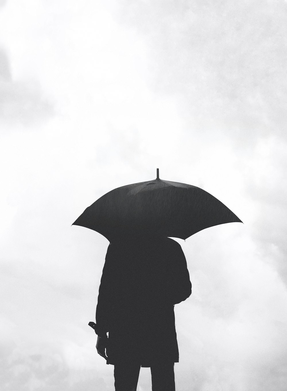 silhouette of person under umbrella under cloudy sky