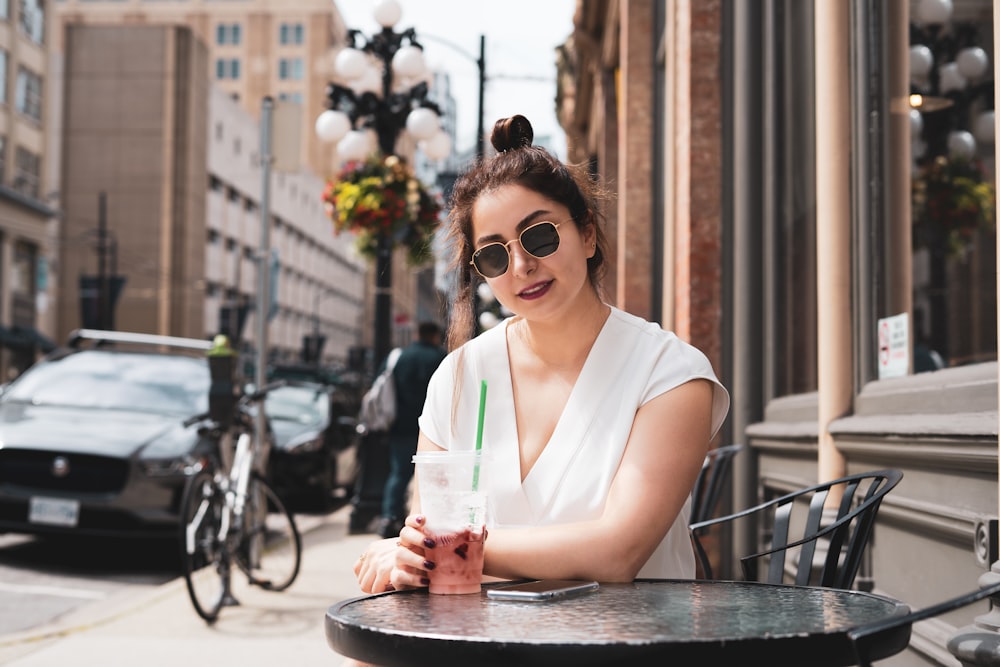 Femme en chemise blanche sans manches portant des lunettes de soleil noires assise sur une chaise