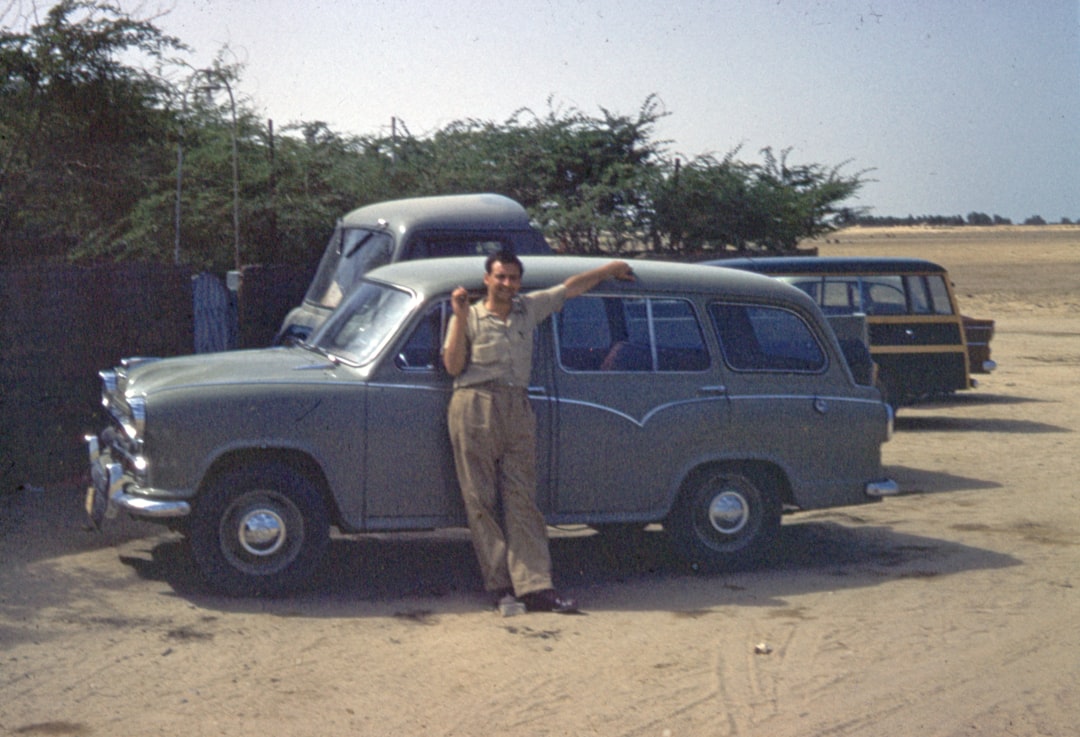 man in brown jacket standing beside black car during daytime
