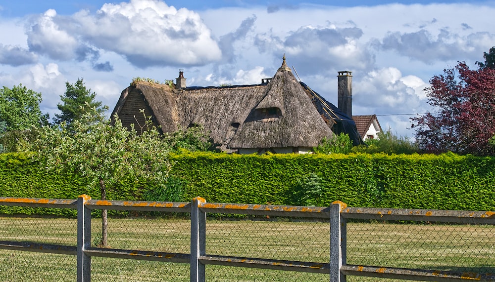 brown wooden fence near green grass field and brown house under white clouds and blue sky