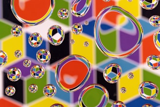 Water droplets of various sizes rest on a surface with a colorful, geometric pattern. The background consists of brightly colored cubes and geometric shapes, creating an optical illusion effect.