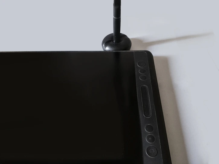 A sleek Huion graphic tablet with a stylus resting on a minimalist white desk.