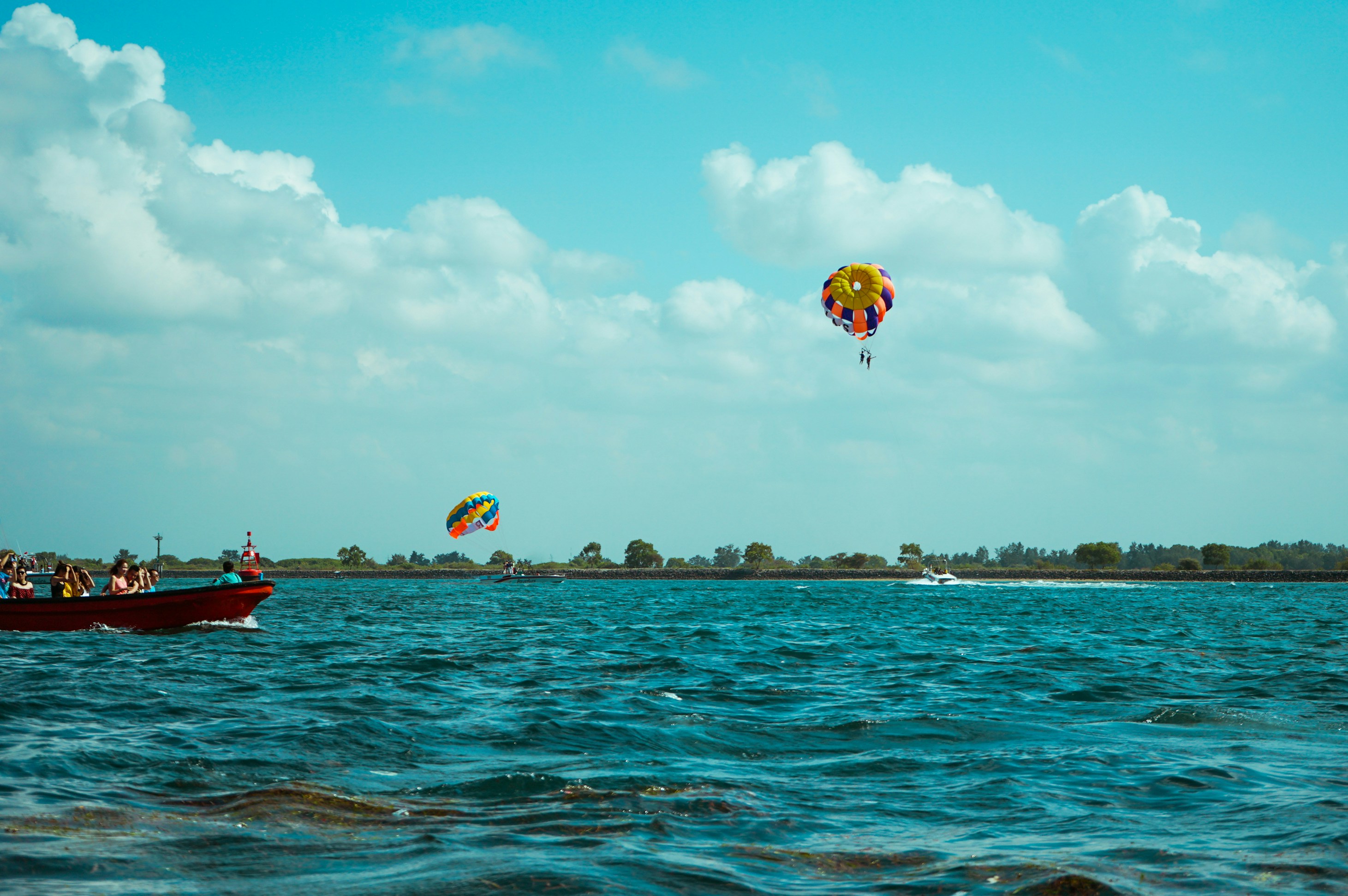 people riding red and yellow parachute over blue sea under blue sky during daytime, Seascape, clouds and marine sports activities in Tanjung Benoa, Bali, Indonesia