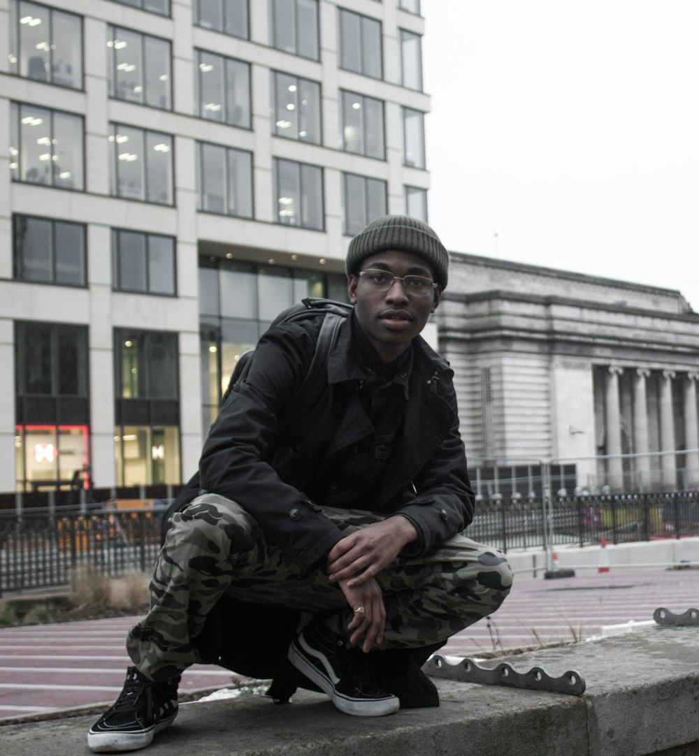 Homme en veste noire et pantalon noir assis sur un banc en béton pendant la journée