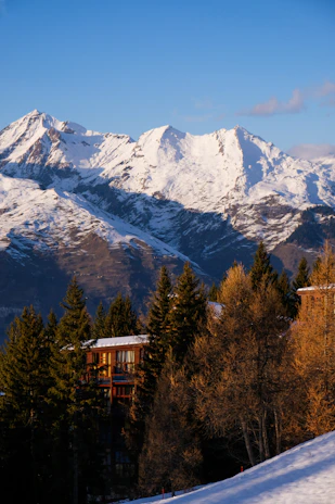 Sunset over the rustic wooden lodge surrounded by pine trees and the Teton mountains in the distance.