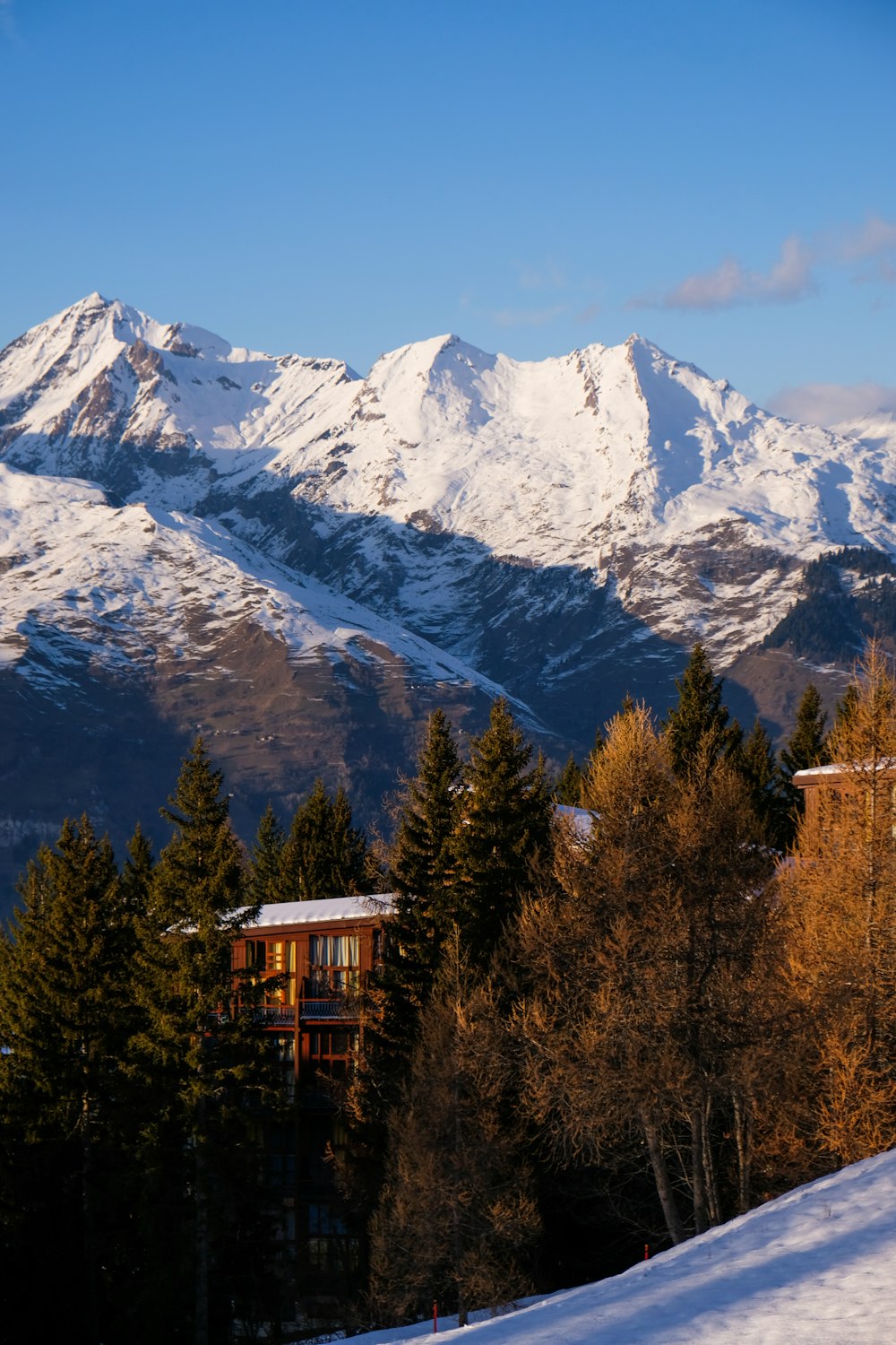 brown wooden house near snow covered mountain during daytime