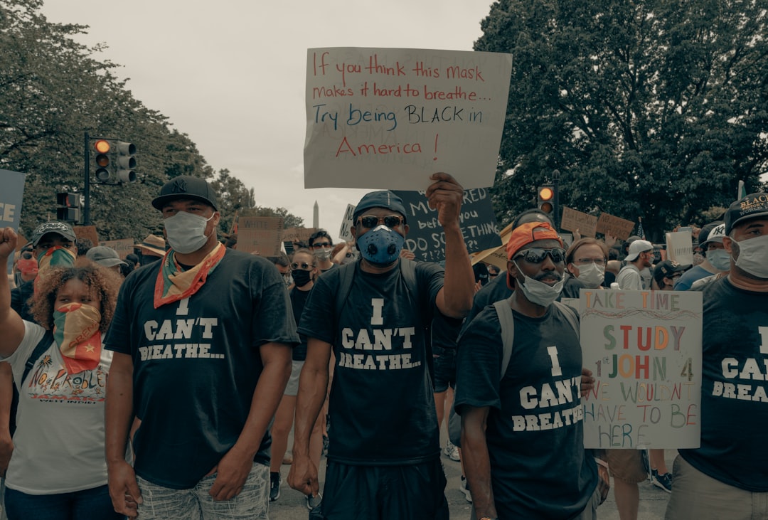 man in blue crew neck t-shirt holding white and red signage, Men stand in unity at the Black Lives Matter protest in Was