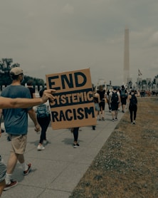 man in gray t-shirt holding black and white welcome to the beach signage