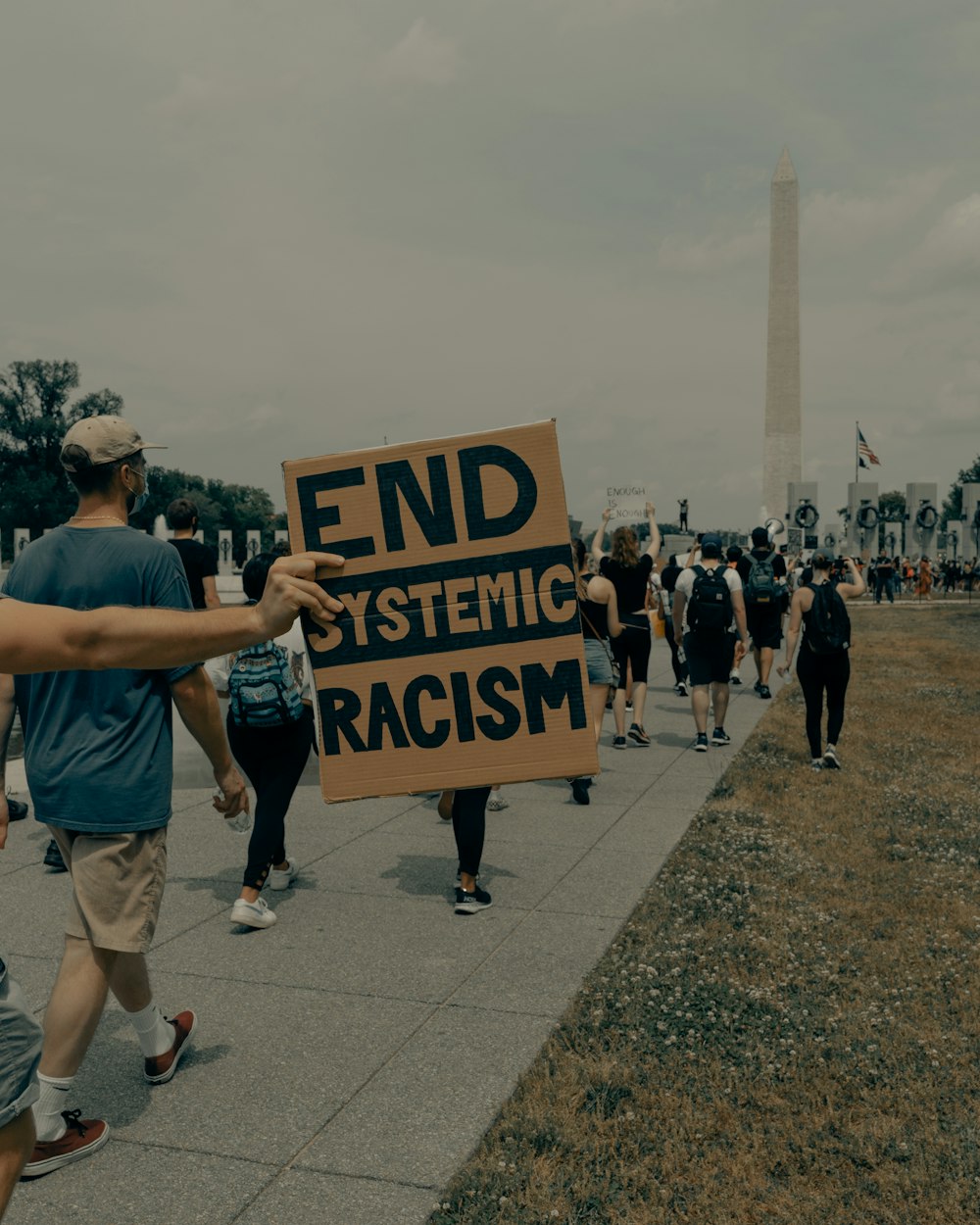 man in gray t-shirt holding black and white welcome to the beach signage