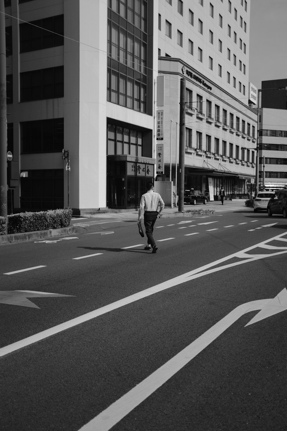 man in white long sleeve shirt and pants walking on pedestrian lane in grayscale photography