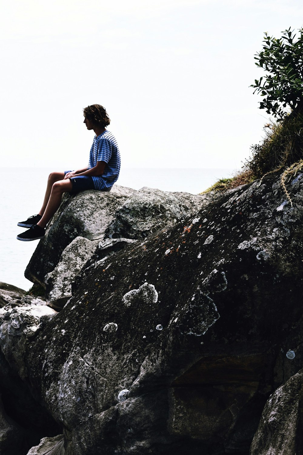 man in blue t-shirt and black shorts sitting on rock near body of water during