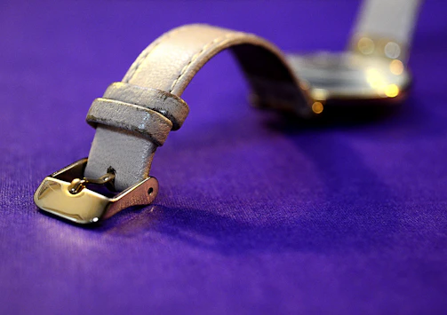 Close-up of a sleek black leather watch strap with fine gold stitching under soft lighting.