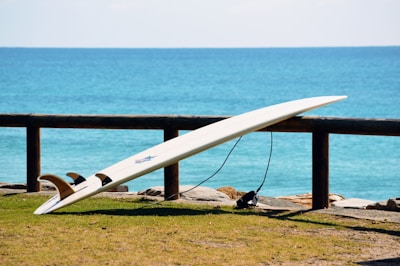 A sleek intermediate surfboard angled against a rocky shoreline under a clear sky