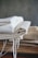 A stack of folded fabric pieces is placed on a wooden surface. The fabrics consist of various natural tones, with some having frayed edges suggesting a handmade or rustic quality. The backdrop is a plain, muted wall that complements the earthy colors of the cloth.