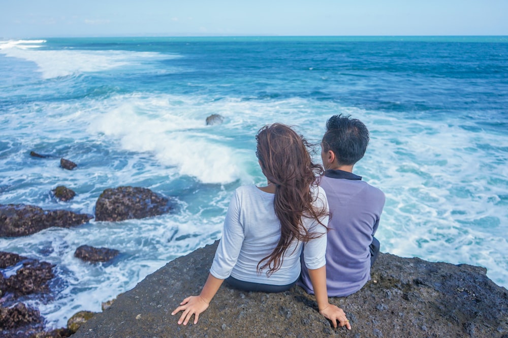 Mujer con camisa blanca sentada en la roca junto al mar durante el día