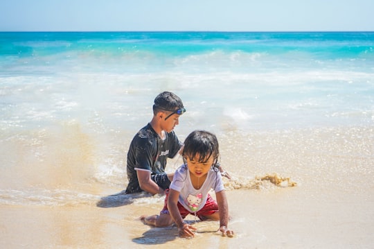 man in black shirt carrying girl in yellow and white tank top on beach during daytime in Dreamland Beach Indonesia