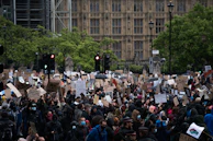 Protesters holding signs and chanting slogans in a city square.