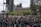 A large crowd of people gathered in a public square, many holding signs and banners advocating for social justice, with the recognizable architecture of a historical building in the background. The atmosphere is bustling, with individuals wearing masks and showing solidarity through their messages.