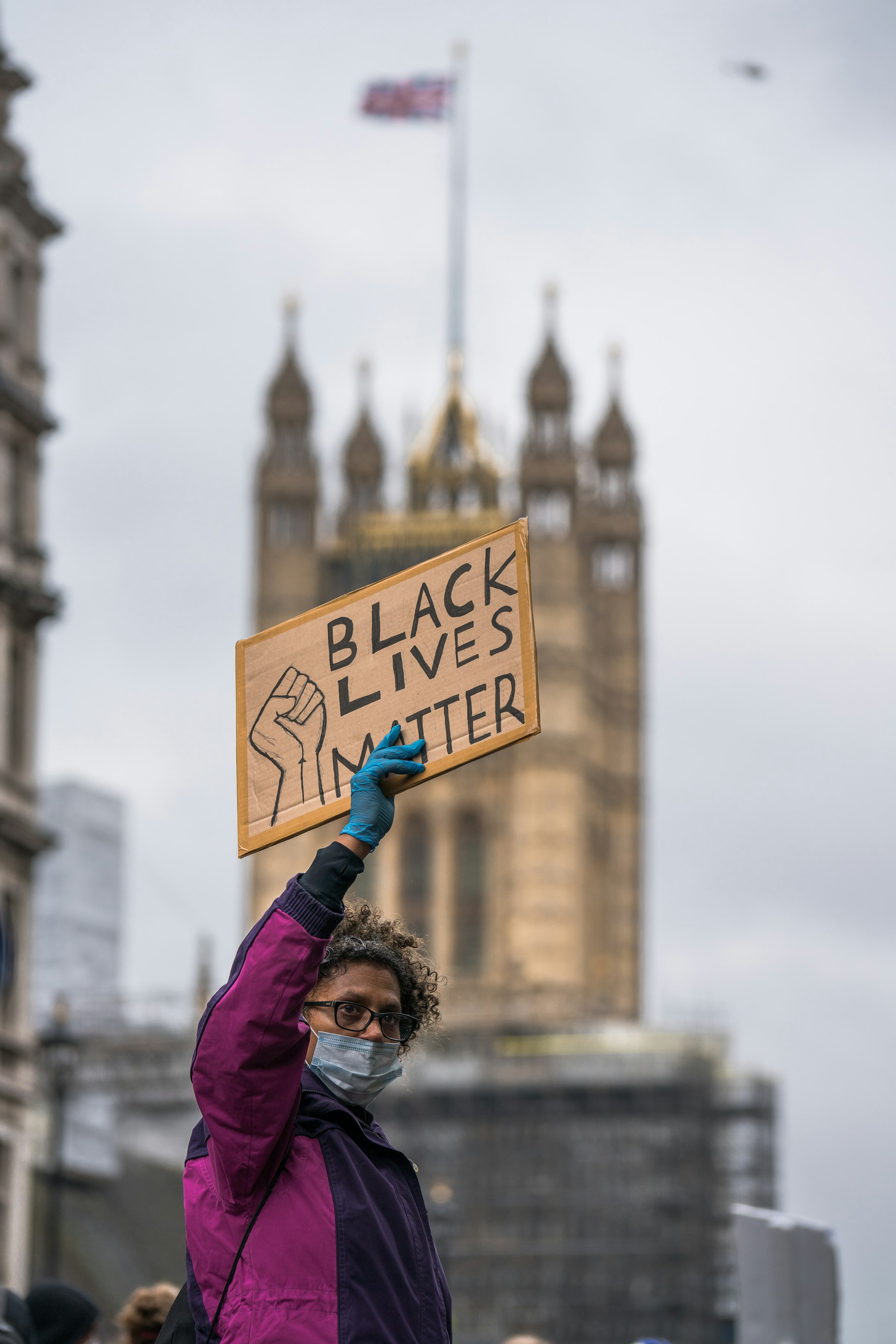 A black woman holding up a Black Lives Matter sign during a Black Lives Matter Protest in London, UK, with the Palace of Westminster in the background.